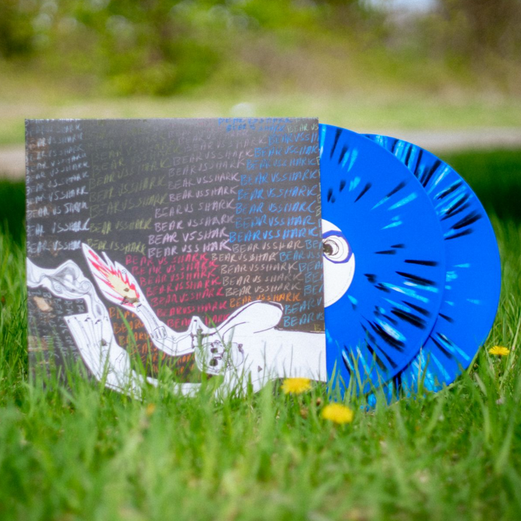 VInyl Cover that depicts a strange looking person with fire and smoke in their hands. Behind them is a chalkboard like texture that has words written on it Those words are Bear vs. Shark over and over again.  There is a vinyl sticking out of the cover and it is colored blue with black and white splatter.  The vinyl is sitting in a grass feild
