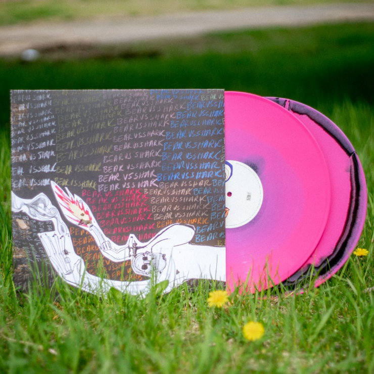 VInyl Cover that depicts a strange looking person with fire and smoke in their hands. Behind them is a chalkboard like texture that has words written on it Those words are Bear vs. Shark over and over again.  There is a vinyl sticking out of the cover and it is colored a mix of pink and black.  The vinyl is sitting in a grass field.