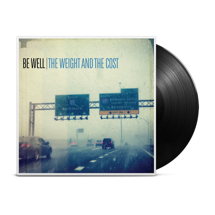 Vinyl jacket with a picture of a highway on a rainy day..  Text on the cover reads BE WELL THE WEIGHT AND THE COST. Sticking out of the vinyl cover is a black record.