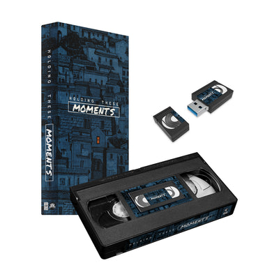 We have a VHS tape that is actually a USB driver device. On the VHS is a picture of a VHS with the text, MOMENTS, in the center of the VHS. The color of dark blue is incorporated into the VHS tape to accent the aesthetic of the tape.