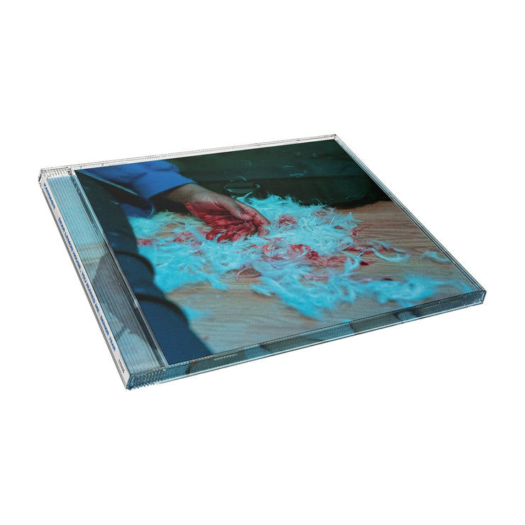 Square CD with an image of a person laying on the ground with their hand covered in blood. Surrounding their hand are white feathers, some covered in blood. All of this is on light wooden flooring.