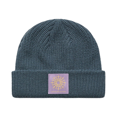 Blue colored winter hat with a purple patch. Inside the patch is a compass / star burst design in white.