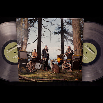 There is a vinyl jacket with a photo of people holding instruments and standing in front of trees. There are amps and percussion instruments behind these people, and a wild animal in the front center of all of it. There are two clear vinyl peeking out from the left and right sides of the vinyl jacket.