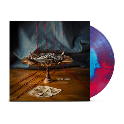 An image of a square LP cover with vinyl disc half exposed. LP cover features a wooden centerpiece positioned on a wooden floor with a blue curtain behind. 4 strands of yarn run behind the centerpiece across the floor. On the centerpiece lies a dead bird and at its base lie 3 playing cards. Vinyl Disc is a blue and red mixed LP
