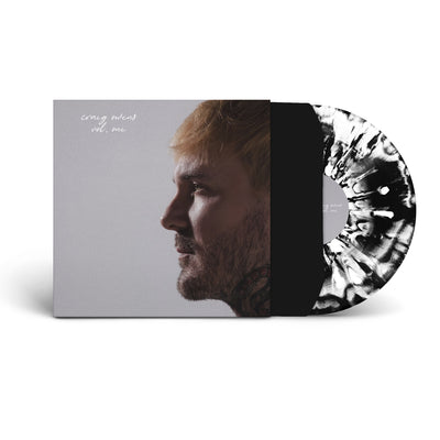 'Volume One' vinyl. A vinyl record is pictured against a white background. The cover of the record is grey, with a man's profile on the right side of it. To the left of him, in the upper corner, are the words "Craig Owens," and below it, "vol. one" in white cursive letters. Behind the album cover is a record in a black slip cover. The record itself is white with black splatters.