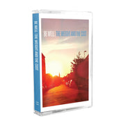 Cassette tape with white text that says BE WELL. Next to that there is blue text that says THE WEIGHT AND THE COST. The album artwork is an image taken down a street while the sun is setting. There are cars lining the street as well as trees and a street light.