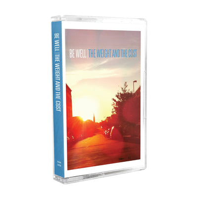 Cassette tape with white text that says BE WELL. Next to that there is blue text that says THE WEIGHT AND THE COST. The album artwork is an image taken down a street while the sun is setting. There are cars lining the street as well as trees and a street light.