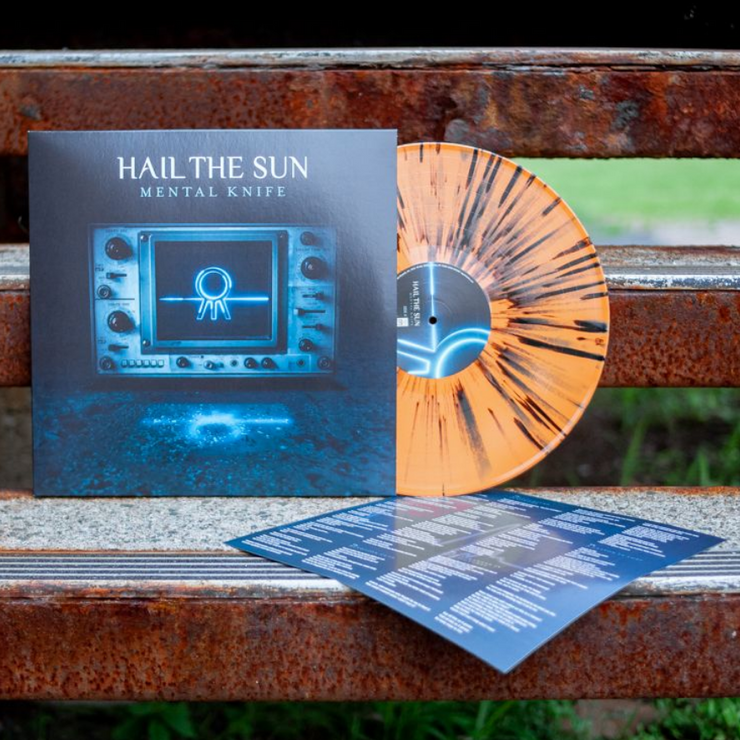 We see a vinyl cover that shows a vintage tv in a poorly lit room with the band’s symbol appearing on screen. There is text on the top center that reads HAIL THE SUN and MENTAL KNIFE below it. Sticking out of the vinyl cover is an orange and black colored vinyl. The vinyl is leaning against a closeup of a park bench. There is green grass shown in the background.