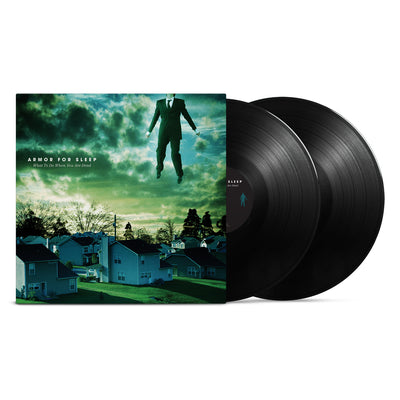 Square vinyl with white text that says ARMOR FOR SLEEP in blue and green tinted clouds. Below that there is smaller text that says WHAT TO DO WHEN YOU ARE DEAD. The album art is an image of a neighborhood of houses. In the top right there is a body of a man wearing a suit, but his head is not in the frame. Two black Records are sticking out of the side.