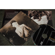 Square CD with a black and white picture of a young person who is blindfolded and shirtless. The person had their hand across their chest and on their heart. To the right of the case is a CD disc with black nails covering it, and GIDEON written in yellow. Below that is text that says COLD.