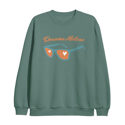 Sage green crewneck with orange text that says DONOVAN MELERO in cursive. Below that is a pair of sunglasses with teal colored frames and orange colored lenses. There is a white heart in both lenses.