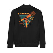 Back of black champion bomber jacket with an orange microphone drawn in the center. Surrounding it is an orange triangle filled with black and teal stripes. On top of the triangle there is orange text that says DONOVAN and on the side there is orange text that says MELERO in cursive.