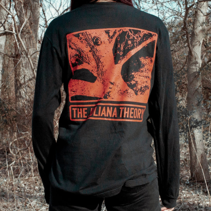 Back of black long sleeve shirt with a drawing of a red tree trunk. Below that there is red text that says THE JULIANA THEORY. An individual is modeling the shirt and standing in the woods in front of dead trees.