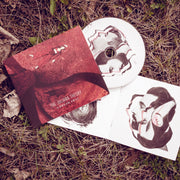 Square CD with art of a girl laying on red ground next to the trunk of a tree. Photo is taken in an aerial above view. Text at the bottom of the CD says THE JULIANA THEORY A DREAM AWAY. Laying under that is a CD disc. The CD disc has images of two male side profiles on a white background. Under that are the same photos on the interior of the CD. All are laying in a patch of grass.