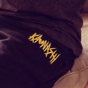 A person is sitting on a couch wearing black sweatpants with text by the waistband that reads Kaonash.
