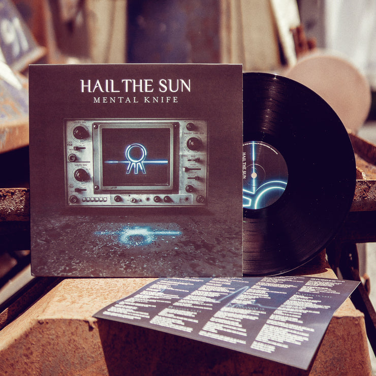 Black vinyl back with white text across the top that says HAIL THE SUN. Below that there is smaller white text that says MENTAL KNIFE. The center of the jacket is an old radio with the Hail The Sun logo in the center in blue (circle with three lines coming out of the bottom). The radio is sitting on a granite reflective surface. There is a black vinyl peeking out of the jacket. Both are being leaned up against a wooden surface.