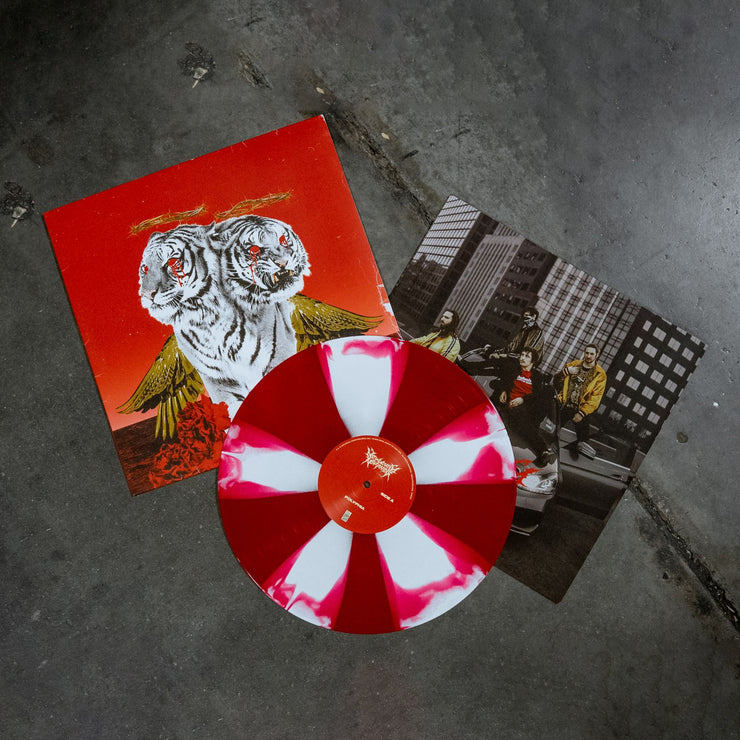 Square vinyl with a red background and a two headed white tiger with gold wings with red roses at the bottom of the cover, blood coming from both tiger’s eyes, and a crown of thorns above both of the tigers heads. There is a vinyl record that is next to the vinyl cover that is the colors red and white. There is also a picture of the band members sitting on top of a car underneath both the vinyl and vinyl cover.  The image is taken with a concrete sidewalk background.