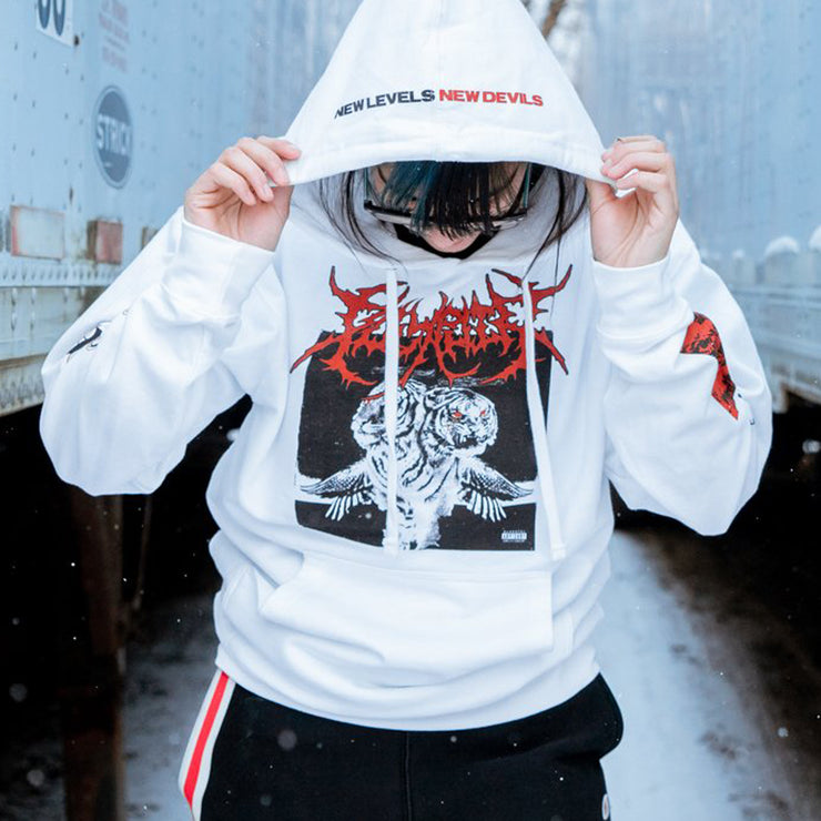 White pullover hoodie with POLYPHIA written in red metal font across the chest. Below the red font there is album artwork of two white tigers with wings and bloody eyes. On the hood there is text that says NEW LEVELS NEW DEVILS. On one arm there is black and red text that says POLYPHIA. An individual is modeling the shirt and standing in between two white trucks.