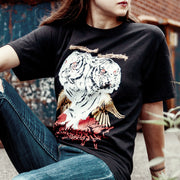 Black short sleeve shirt with two white tigers in the center. The tigers have yellow wings and red dripping from their eyes. The tigers are on top of red text that says NEW LEVELS NEW DEVILS. A model is sitting and wearing the shirt in front of a brick building.