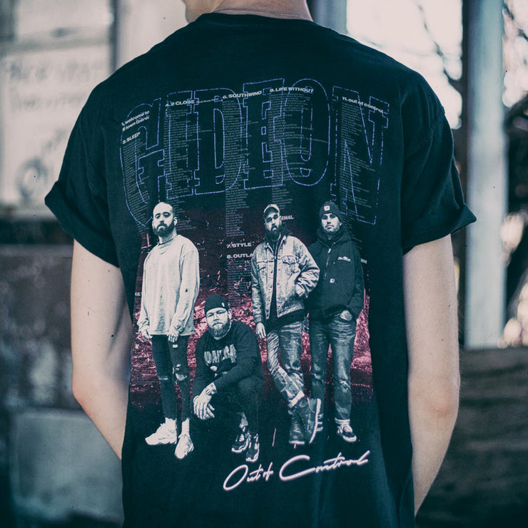 Back of black short sleeve shirt with an image of the band members. Behind the image there is text of song lyrics. An individual is modeling the shirt and standing outside.
