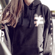 Black pullover hoodie with a not equal to sign in the top corner. On one sleeve there is text that says VAGRANTS. In the other sleeve there is text that says SEPARATION. An individual is modeling the hoodie.