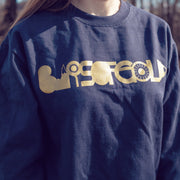 Navy crewneck with BARS OF GOLD written across the chest in gold lettering. Crewneck is being worn by an individual standing outside in front of a forest.