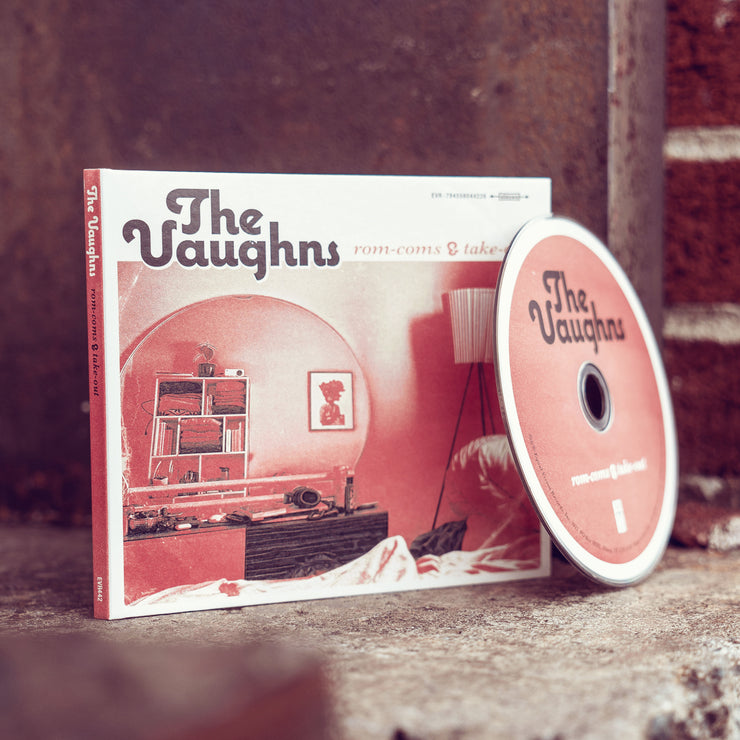 Square CD with The Vaughns written in the top left corner in black font. To the right of that, there is smaller red text that says rom-coms & takeout. The album art is a drawing of a 70's living room with a large rounded arch in the center. The drawing is done in white, black, and red. A CD disc is leaning up against the cover. The disc is the same red color as the album. 
