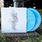 White vinyl jacket with a "taped" on image of a ballerina in the center. To the right of the vinyl jacket is a blue and white mix vinyl. The vinyl jacket and vinyl are propped up in top a concrete block, on top of grass.