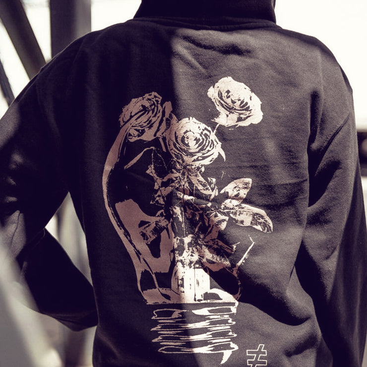 Back of black pullover hoodie with a large broken light bulb being used as a vase, with flowers coming out of it. An individual is modeling the hoodie.