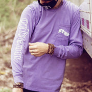 Violet colored long sleeve shirt with a pocket in the top corner, with OUT OF CONTROL written in wavy white font. On one of the arms there is white text that says GIDEON down the side. An individual is modeling the shirt and leaning against a white truck.
